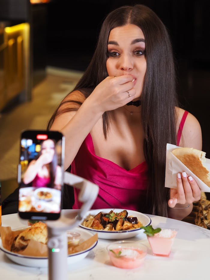 A young woman enthusiastically blogs about food while eating in a stylish restaurant.