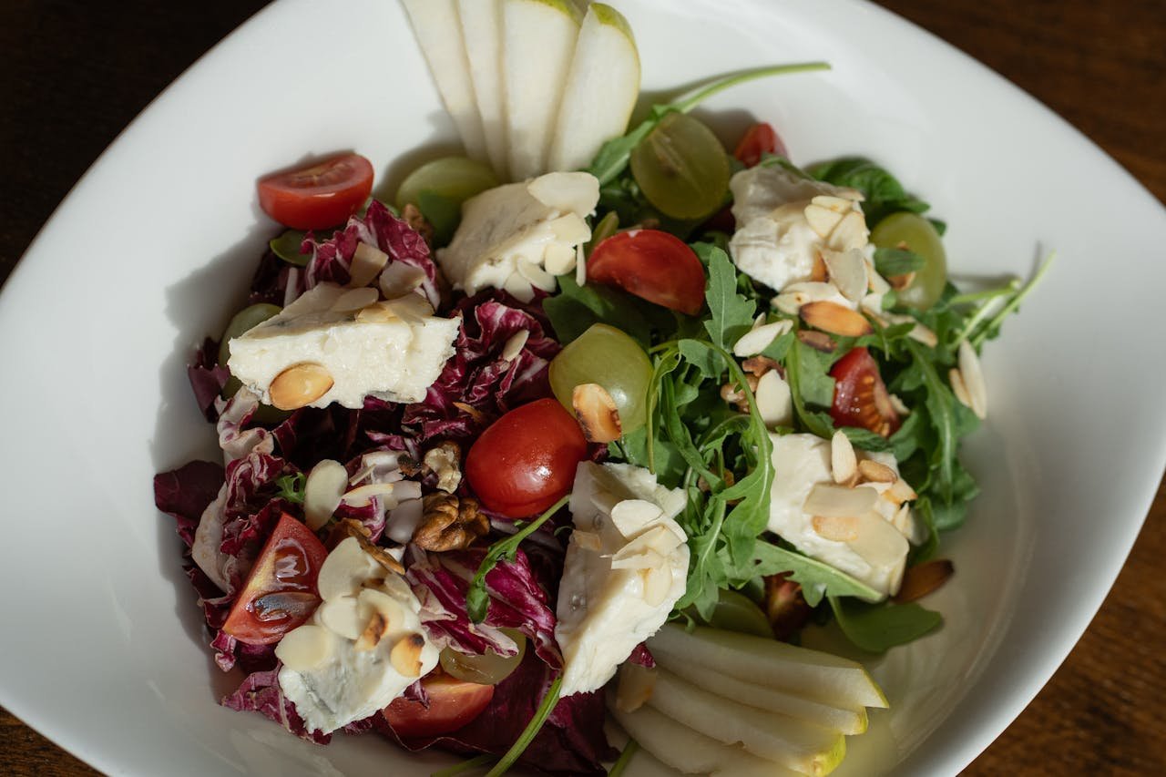 Colorful salad with brie cheese, grapes, and almonds on a white plate.